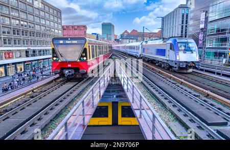 Züge nähern sich dem Alexanderplatz im Zentrum von Berlin. Unten befindet sich eine gelbe BVG-Straßenbahn. Stockfoto