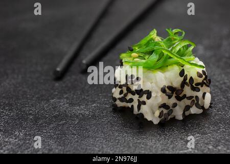 Sushi mit grünen Algen. Essensstäbchen. Schließen. Schwarzer Hintergrund Stockfoto