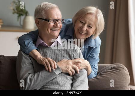 Positives älteres pensioniertes Paar, das sich auf dem Sofa umarmt Stockfoto