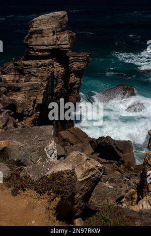 Die Wellen des Atlantiks unter einem geschichteten Felsen oder Meerespfeiler, einer von vielen, die durch Wellen und Wind entlang der zerklüfteten Küste von Cabo Carvoeiro in Peniche im Stadtteil Leiria im Zentrum Portugals in seltsame Formen geformt wurden. Ein Großteil des Sedimentgesteins wurde in der frühen Jurassic Epoche vor bis zu 200 Millionen Jahren gelegt. Stockfoto