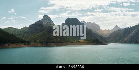 Panoramablick auf den gipfel des gilbo und seine nahen Berge am stausee Riaño gelegen, erhellen türkisfarbene Gewässer unter dem blauen Himmel die Gipfel Stockfoto