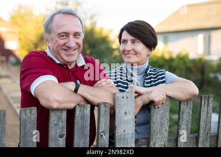 Ein älteres Paar, das in der Nähe eines Holzzauns im Garten steht Stockfoto