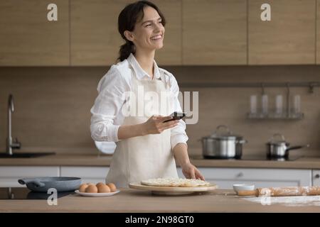 Fröhliche Bäckerei-Bloggerin mit Smartphone am Tisch Stockfoto