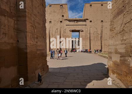 Der Tempel von Edfu in Edfu, ägyptischer Blick bei Tageslicht, der den Haupteingang mit Besuchern und Wolken am Himmel im Hintergrund zeigt Stockfoto