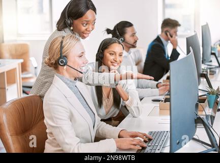 Sie ist eine tolle und hilfsbereite Führungskraft. Eine Gruppe weiblicher Callcenter-Agenten, die Headsets tragen und an einem Computer im Büro zusammenarbeiten. Stockfoto