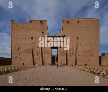 Der Tempel von Edfu in Edfu, ägyptischer Blick bei Tageslicht, der den Haupteingang mit Besuchern und Wolken am Himmel im Hintergrund zeigt Stockfoto