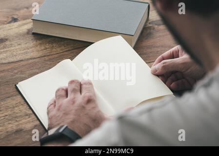 Über der Schulter gesehen, wie eine Person auf einem Holztisch sitzt und ein Buch liest Stockfoto