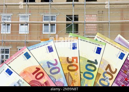 Renovierung alter Gebäude und Zuschüsse. Renovierungskosten - Euro-Scheine mit nicht renoviertem Gebäude im Hintergrund Stockfoto