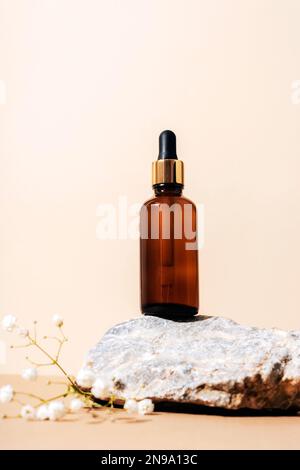 Braunglasserumflasche auf Naturstein mit Zigeunerblüten. Neutraler beigefarbener Hintergrund. Schönheit, Hautpflegekonzept. Stockfoto