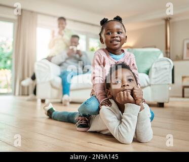 Wer ist besser als dein Bruder. Die volle Länge eines bezaubernden kleinen Mädchens, das auf ihren Brüdern zu Hause auf dem Wohnzimmerboden sitzt. Stockfoto