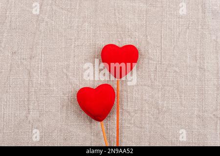 Zwei rote Herzen auf grauem Stoffhintergrund. Valentinstag-Konzept. Draufsicht, flach liegend. Stockfoto