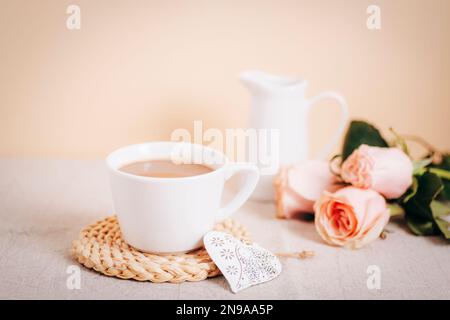 Eine Tasse Kaffee, ein altes Spielzeugherz, rosa Rosen und eine Kanne mit Milch auf einem Tisch. Valentinstag-Konzept. Frühstück am Morgen. Schließen. Stockfoto