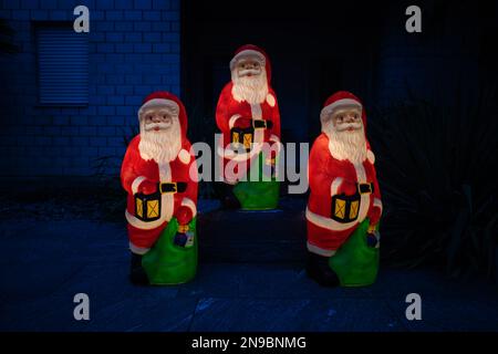 Figuren von drei Weihnachtsmännern bei Nacht mit Lampen im Hof des Hauses Stockfoto