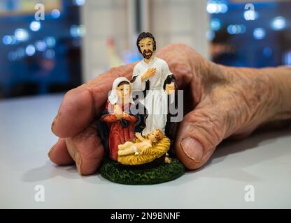 Die Hand einer alten Frau hält eine Miniatur von Weihnachtsbetten - Krippenszene Stockfoto