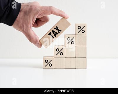 Steuererhöhung oder Steuerinflation. Die Hand legt einen Holzblock mit dem Wort Steuer auf Holztreppen mit Prozentsymbolen. Stockfoto