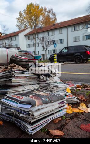 Zürich, Schweiz - 17. November 2022: Ein Haufen gefesselter Zeitungen zum Recycling auf der Straße und ein vorbeifahrendes Auto Stockfoto