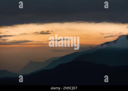 Die französischen Alpen nach Sonnenuntergang, Schichten von Bergen und weicher, pastellfarbener, pfirsichfarbener Himmel mit dunklen Wolken, matte Technik, horizontal Stockfoto