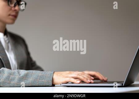 Geschäftsfrau mit Brille sitzt am Schreibtisch im Büro mit einem Laptop. Vorlage arbeitet an Laptop. Stockfoto