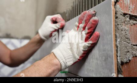 Installation von Keramikfliesen. Männliche Hände kleben Keramikfliesen an die Wand im Badezimmer. Stockfoto