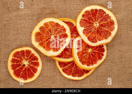 Mehrere trockene Grapefruitscheiben auf Jutetuch, Makro, Draufsicht. Stockfoto