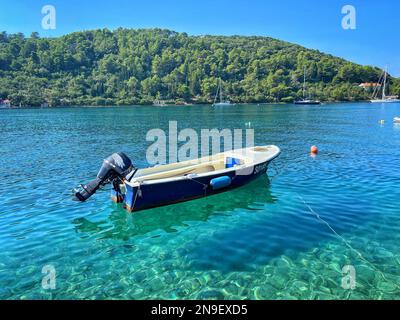 Ein festsitzendes Segelboot, das in einem türkisfarbenen Meer mit tropischer Vegetation im Hintergrund in Kroatien schwimmt Stockfoto