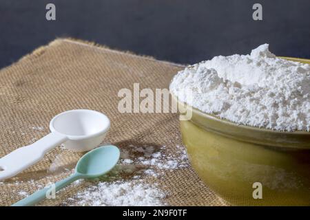 Allzweckmehl in einer Keramikschüssel mit Messlöffel, Allzweckmehl und Eier können zur Herstellung einer Vielzahl von Backwaren und anderen Gerichten verwendet werden. Stockfoto