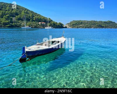 Ein festsitzendes Segelboot, das in einem türkisfarbenen Meer mit tropischer Vegetation im Hintergrund in Kroatien schwimmt Stockfoto