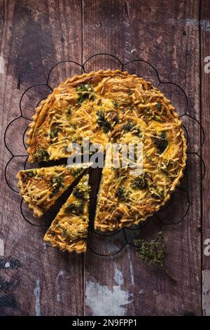 Blick von oben auf eine köstliche Brokkoli-Quiche auf einem Holztisch, mit zwei ausgeschnittenen Scheiben Stockfoto