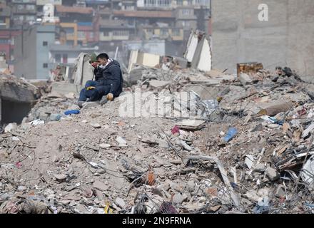 Kahramanmaras, Türkei. 12. Februar 2023. Zwei Männer sitzen auf einem Berg voller Trümmer. Fast eine Woche nach der Erdbebenkatastrophe in der türkisch-syrischen Grenzregion ist die Zahl der Toten auf über 30.000 gestiegen. Kredit: Boris Roessler/dpa/Alamy Live News Stockfoto