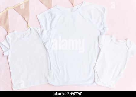 Weißes Modell-T-Shirt und Einteiler für Babys mit pastellrosafarbenem Hintergrund für Eltern und Kinder. Stockfoto