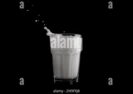 Milchtropfen in einem Glas auf schwarzem Hintergrund. Stockfoto