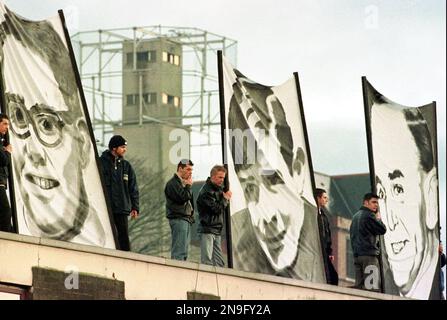 File - Protestors hold banners showing portraits of three of the thirteen killed on Bloody Sunday, against a backdrop of a security tower in this Sunday, Feb. 1, 1998 file photo, in Londonderry, Northern Ireland. The rally was held to honor the Irish demonstrators killed during a civil rights march in 1972. Chief Constable Matt Baggott told Northern Ireland’s policing board Thursday July 5 2012 that his force is planning a Bloody Sunday investigation that would require 30 detectives and take four years. Northern Ireland’s police commander says his detectives will eventually investigate the Blo