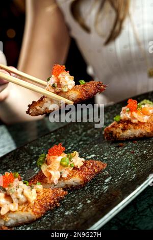 Ein vertikaler Schuss Stäbchen, der ein knuspriges Reislachs-Sushi-Brötchen aufnimmt Stockfoto