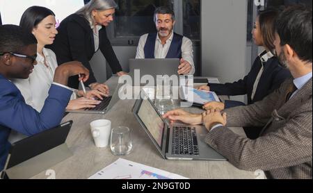 Erfolgreicher Teamleiter und Unternehmer, der ein informelles internes Geschäftstreffen leitet. Geschäftsmann, der im Vordergrund an einem Notebook arbeitet. Unternehmerisch Stockfoto