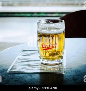 Ein Becher voller Bier steht an der Speisekarte am Tisch auf dem Bahnsteig des Bahnhofs Ljubljana. Logo der Slowenischen Union für Bier auf der Tasse. Stockfoto