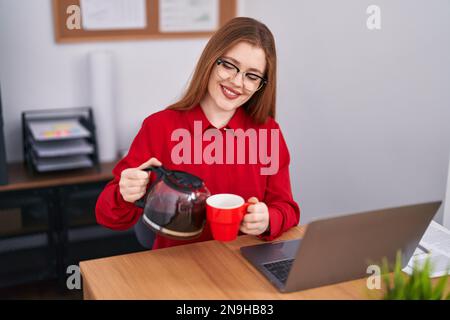 Junge Rothaarige Geschäftsarbeiterin, die im Büro Kaffee auf die Tasse gießt Stockfoto
