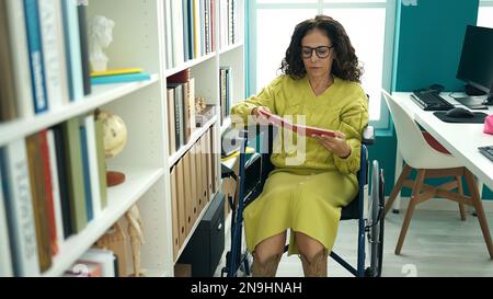 mittelalterliche hispanische Lehrerin, die an der Bibliotheksuniversität im Rollstuhl Buch liest Stockfoto