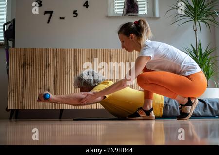 Professionelle Physiotherapeutin, die mit einem älteren Mann arbeitet und ihm Übungen für den Rücken zeigt, um fit zu bleiben. Stockfoto