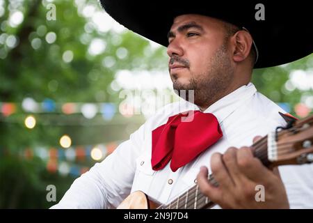 Mexikanischer Musiker Mariachi mit Gitarre auf verschwommenem Partyhintergrund Stockfoto