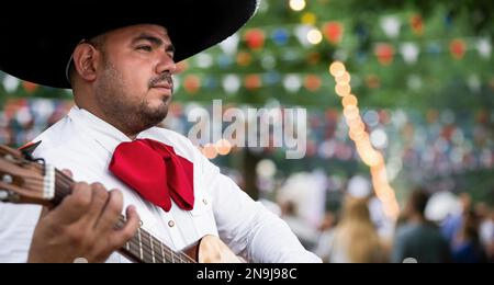 Mexikanischer Musiker Mariachi mit Gitarre auf verschwommenem Partyhintergrund Stockfoto