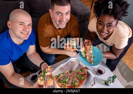 Eine Gruppe junger Freunde, die Pizza essen. Heimmannschaft. Großer Blickwinkel. Ich schaue in die Kamera. Stockfoto