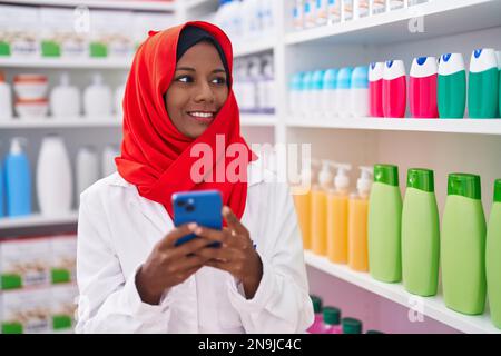 Junge, schöne Apothekerin mit Smartphone, die in der Apotheke arbeitet Stockfoto