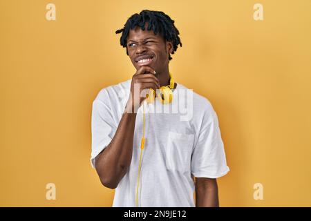 Junger afrikanischer Mann mit Dreadlocks, der über gelbem Hintergrund steht und über eine Frage besorgt denkt, besorgt und nervös mit der Hand am Kinn Stockfoto