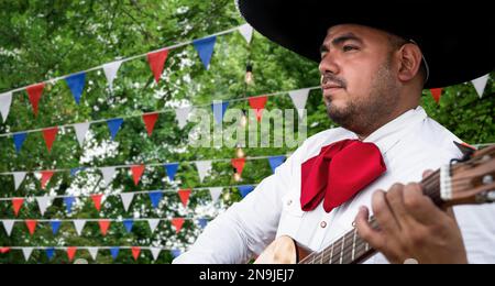 Mexikanischer Musiker Mariachi mit Gitarre auf verschwommenem Partyhintergrund Stockfoto