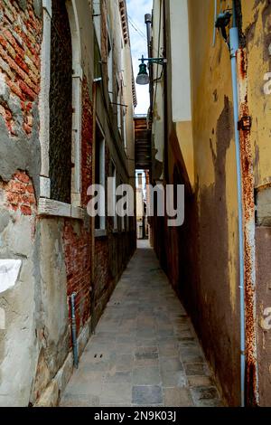 Ein vertikales Bild einer wirklich engen Gasse mit alten Backsteinmauern an den Seiten in Venedig, Italien Stockfoto