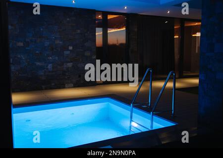 Tauchbecken mit kaltem Wasser, das nach dem Entspannen in der Sauna zubereitet wird. Der Pool ist mit Wasser gefüllt. Abendfoto mit Hintergrundbeleuchtung Stockfoto