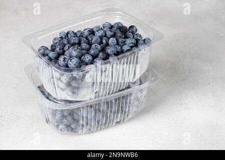 Frische Heidelbeeren in Kunststoffbehältern auf grauem Hintergrund zur Vorbereitung der Beeren zum Einfrieren Stockfoto