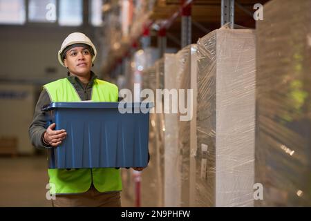 Porträt einer Arbeiterin, die eine Plastikbox im Lager trägt, Kopierraum Stockfoto