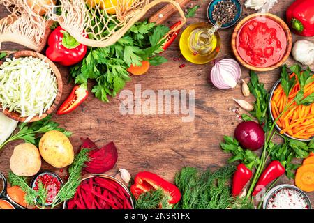Verschiedene ungekochte Gemüsesorten, Kräuter und Gewürze für gesundes Kochen auf rustikalem Küchentisch aus Holz, Rahmen von oben. Zubereitung vegetarischer Kohl, Rüben Stockfoto