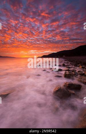 Dramatischer Sonnenaufgang mit leuchtenden rosa Wolken und Nebel über der Küste am Meer von Cortez in der Nähe von La Paz, Mexiko Stockfoto